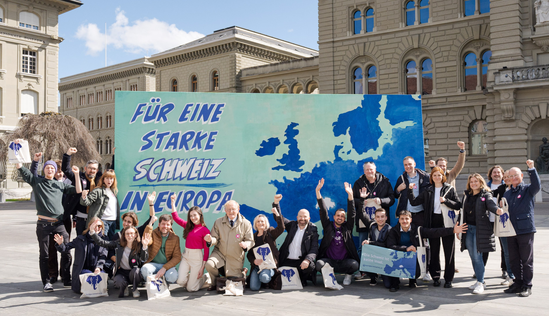 Die Europa-Allianz bestehend aus Vertreter:innen von Volt, Operation Libero, den Grünen, der Europäischen Bewegung Schweiz, VSS und weiteren vor einer Leinwand auf dem Bundesplatz. Die Leinwand zeigt eine Karte Europas, mit der fehlenden Schweiz in der Mitte. Links steht die Aufschrift: 