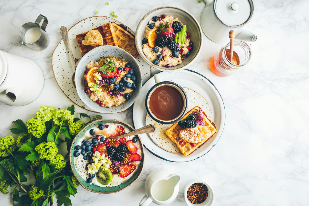 Aufnahme eines gedekten Frühstückstisches mit Müsli, Waffeln, Kaffe und Honig aus der Vogelperspektive.